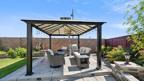 A covered patio area with outdoor furniture, a pergola, and a brick wall in the background. - Spacious 3br Home With Charming Backyard 3 Bedroom Home (Folsom)