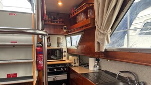 A compact kitchen with a stove, microwave, and sink. There is a gas locker sign and a fire extinguisher visible. - Riverside Boat Retreat on the River Thames (Windsor)