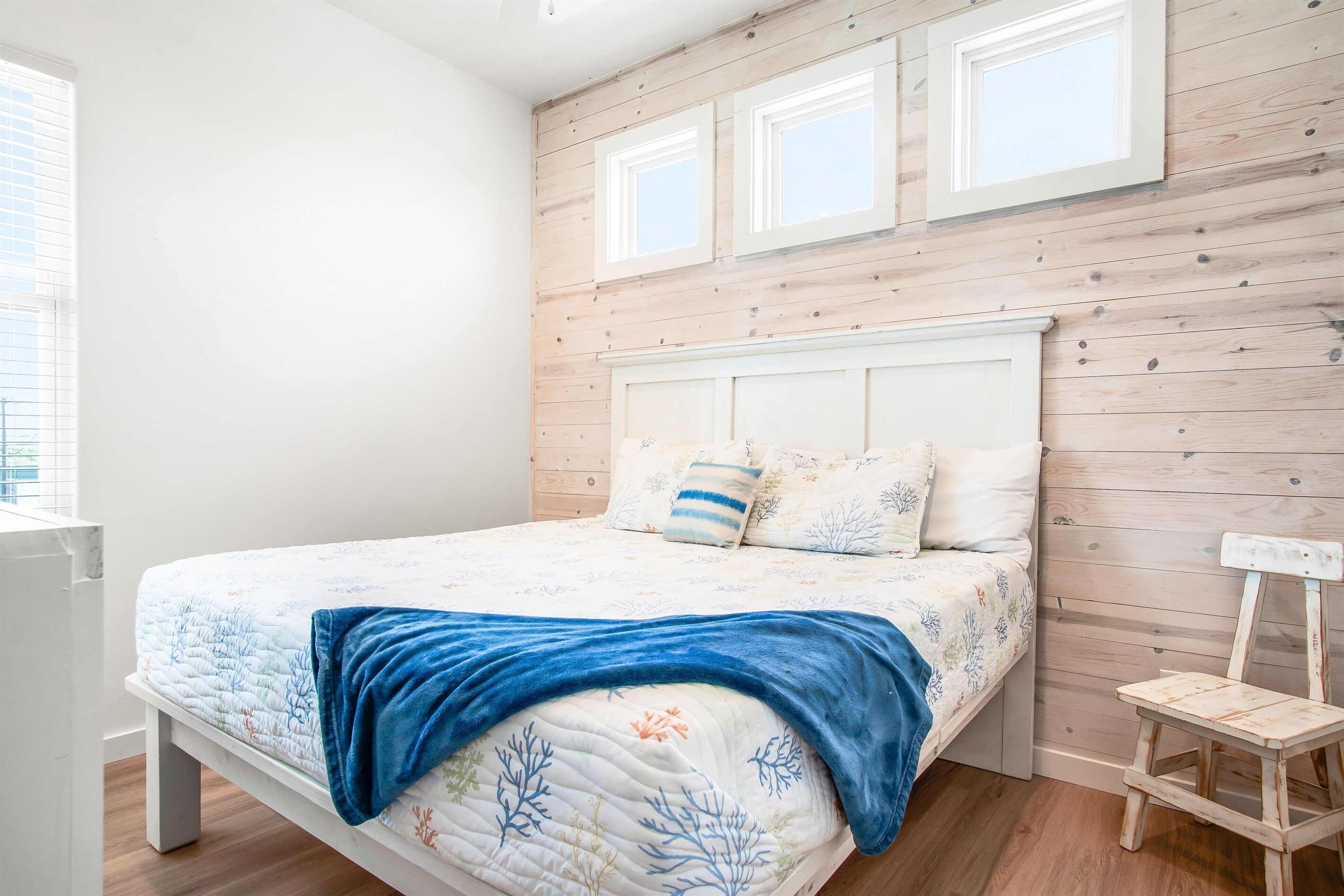 Une chambre à coucher avec un lit, une table de chevet, un banc en bois et une fenêtre avec des stores.