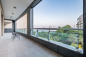 A balcony with a glass railing, a table with chairs, and a view of a cityscape and greenery. - Waterfront 2BR with Assistant Room in Dream Palm Residence, Palm Jumeirah (Dubai)