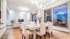 Ein moderner Essbereich mit einem Glastisch, weißen Stühlen und einem Fernseher im Hintergrund.