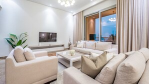 Ein modernes Wohnzimmer mit einer Sofagarnitur, einem Couchtisch, einem Fernseher und einem großen Fenster mit Vorhängen.