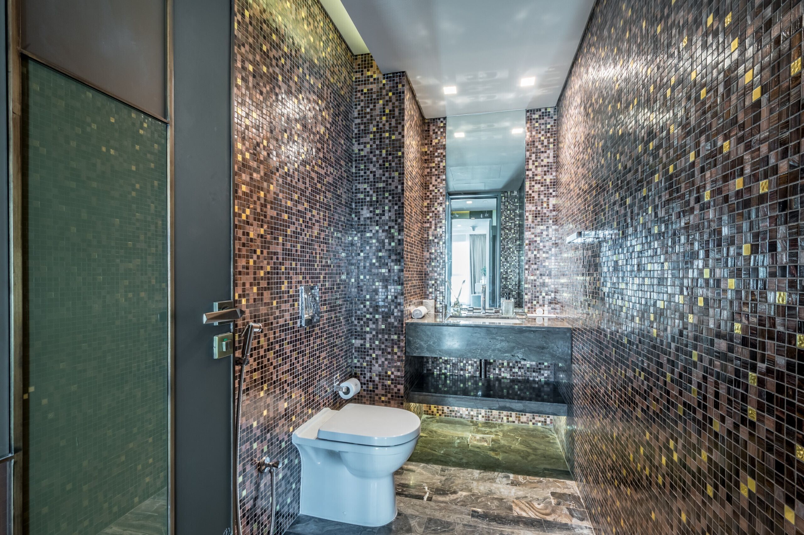A narrow bathroom with mosaic tile walls, a toilet, and a sink.