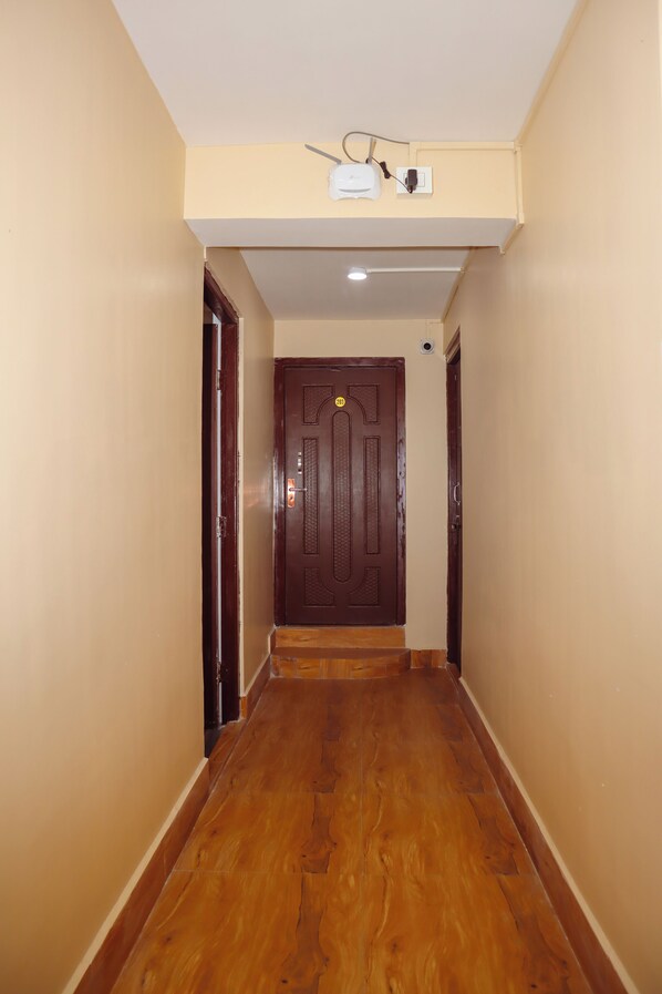 A hallway with wooden flooring, beige walls, and a dark wooden door at the end.