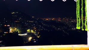 A nighttime cityscape with illuminated buildings and a balcony with a decorative railing.