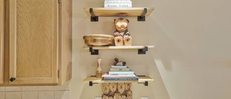Une cuisine avec des meubles de rangement en bois, une étagère remplie de livres, un ours décoratif et une pancarte au-dessus de l’étagère.