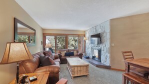 A cozy living room with a fireplace, leather sofa, wooden coffee table, and a dining table. - Beautiful 2 bdrm condo in Breckenridge, Steps to gondola/Main Street! (Breckenridge)