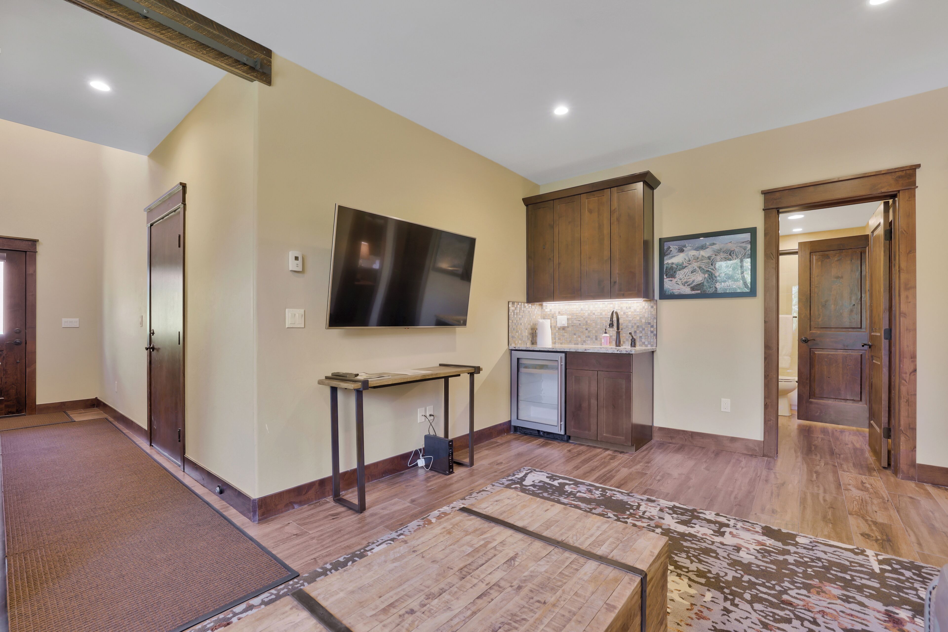 A spacious living area with a flat-screen TV, wooden cabinets, a small refrigerator, and a dining table.