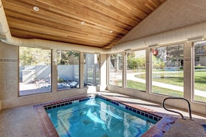 An indoor swimming pool with a wooden ceiling, large windows, and a view of a backyard.