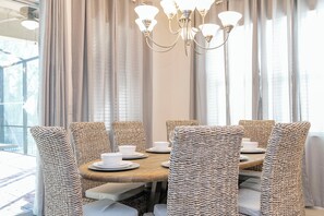 Enjoy meals in this inviting dining area with a round table and six chairs, set with white tableware and illuminated by a chandelier.