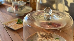 A wooden table with a glass cloche over a plate of sliced bread, a glass jar, and a small dish with a garnish. - Sun Valley Farm Guest House (Chegutu)