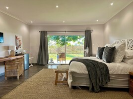 Un dormitorio con una cama grande, un escritorio y una silla. Se ve un jardín a través de la ventana.