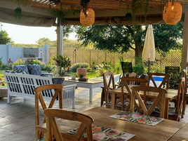 Un patio al aire libre con mobiliario de madera, piscina y abundante vegetación.