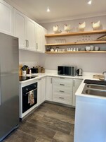 Una cocina moderna con armarios blancos, un refrigerador de acero inoxidable, un microondas y un lavamanos doble.