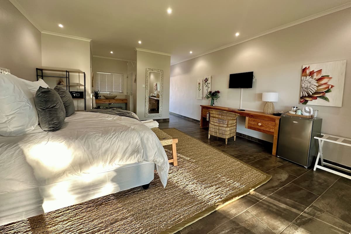 Quarto moderno com uma cama grande, uma escrivaninha, uma cadeira, uma televisão e um frigorífico.