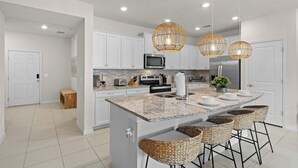 A modern kitchen with white cabinets, granite countertops, a central island with bar stools, and pendant lighting. - Relax in Style with Private Pool, BBQ and More (Davenport)