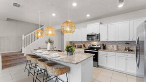 A modern kitchen with white cabinets, a granite countertop, a stainless steel refrigerator, and a built-in oven. - Relax in Style with Private Pool, BBQ and More (Davenport)