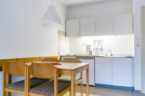 Cocina compacta con gabinetes blancos, una mesa de comedor con sillas y una lámpara colgante.