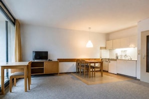 Ein kleines Hotelzimmer mit Küchenzeile, Essbereich, Fernseher und großem Fenster.