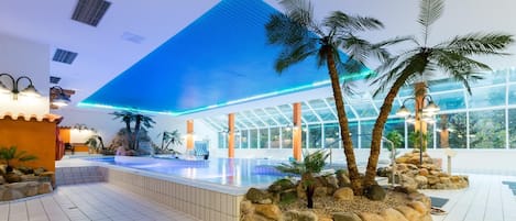 Un moderno vestíbulo de hotel con una gran piscina, palmeras y una zona con paredes de vidrio.