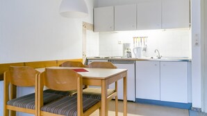 Cocina compacta con gabinetes blancos, una mesa de comedor con sillas y una lámpara colgante.