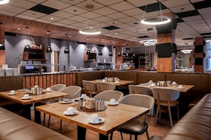Un restaurant moderne avec des tables et des banquettes en bois, un coin bar et des luminaires suspendus.
