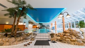 Zona de piscina interior con vista despejada, rodeada de rocas y palmeras.