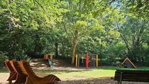 Un parque infantil con toboganes y estructuras para escalar, rodeado de árboles.