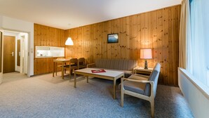 Habitación compacta con una mesa de comedor, dos sillas, un sofá y un televisor instalado en la pared.