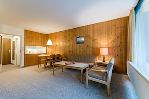 Habitación compacta con una mesa de comedor, dos sillas, un sofá y un televisor instalado en la pared.