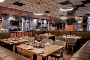 Ein modernes Restaurant mit Holztischen, Sitzbänken, einer Bar und Pendelleuchten.