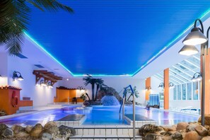 Ein überdachter Pool mit Wasserfall, umgeben von Felsen und Palmen, ausgestattet mit zeitgemäßer Beleuchtung.