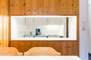 A modern kitchen with wooden cabinetry, white tiles, and a built-in window above the counter.