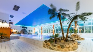 Un moderno vestíbulo de hotel con una gran piscina, palmeras y una zona con paredes de vidrio.