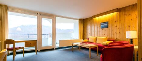 Habitación de hotel con sofá, sillón, mesa y vistas al exterior.