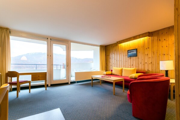 Habitación de hotel con sofá, sillón, mesa y vistas al exterior.