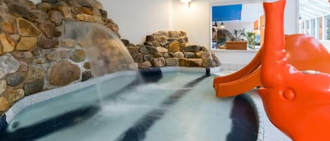 Un jacuzzi con cascada, rodeado por un muro de piedra y una escultura de color naranja brillante.