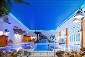 Ein überdachter Pool mit Wasserfall, umgeben von Felsen und Palmen, ausgestattet mit zeitgemäßer Beleuchtung.