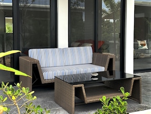 A wicker sofa with striped cushions, a glass coffee table, and a small potted plant. - Solindo Stays (Cuajiniquil)
