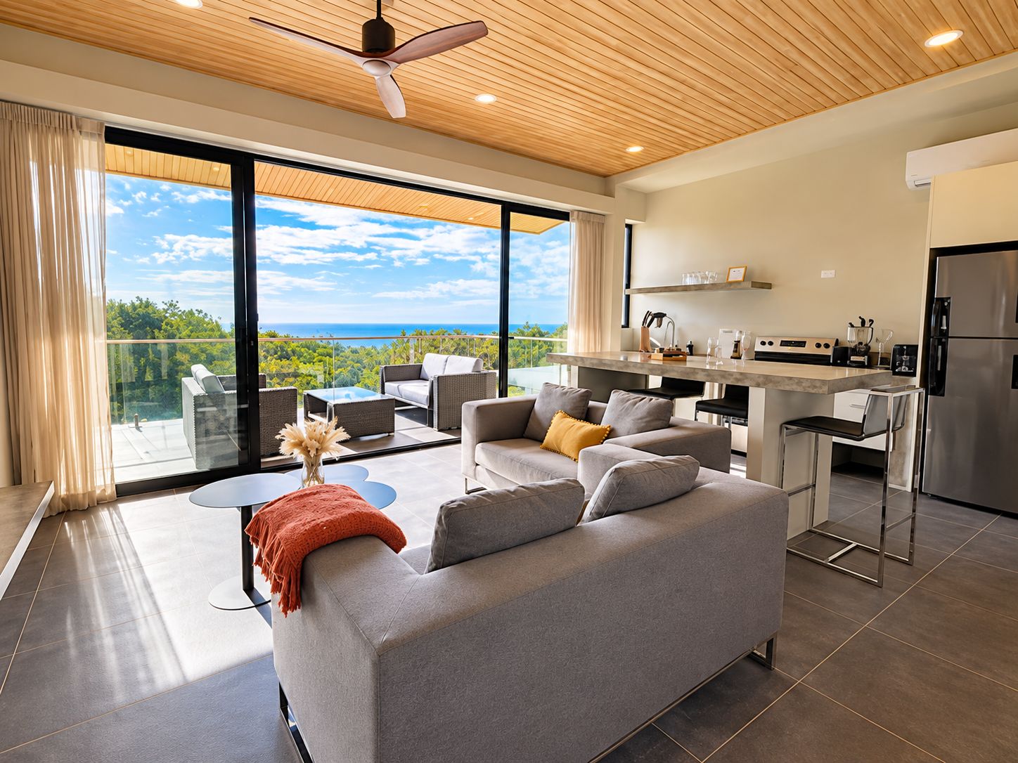 Ein modernes Wohnzimmer mit einem grauen Sofa, einem Couchtisch und Meerblick durch große Fenster.