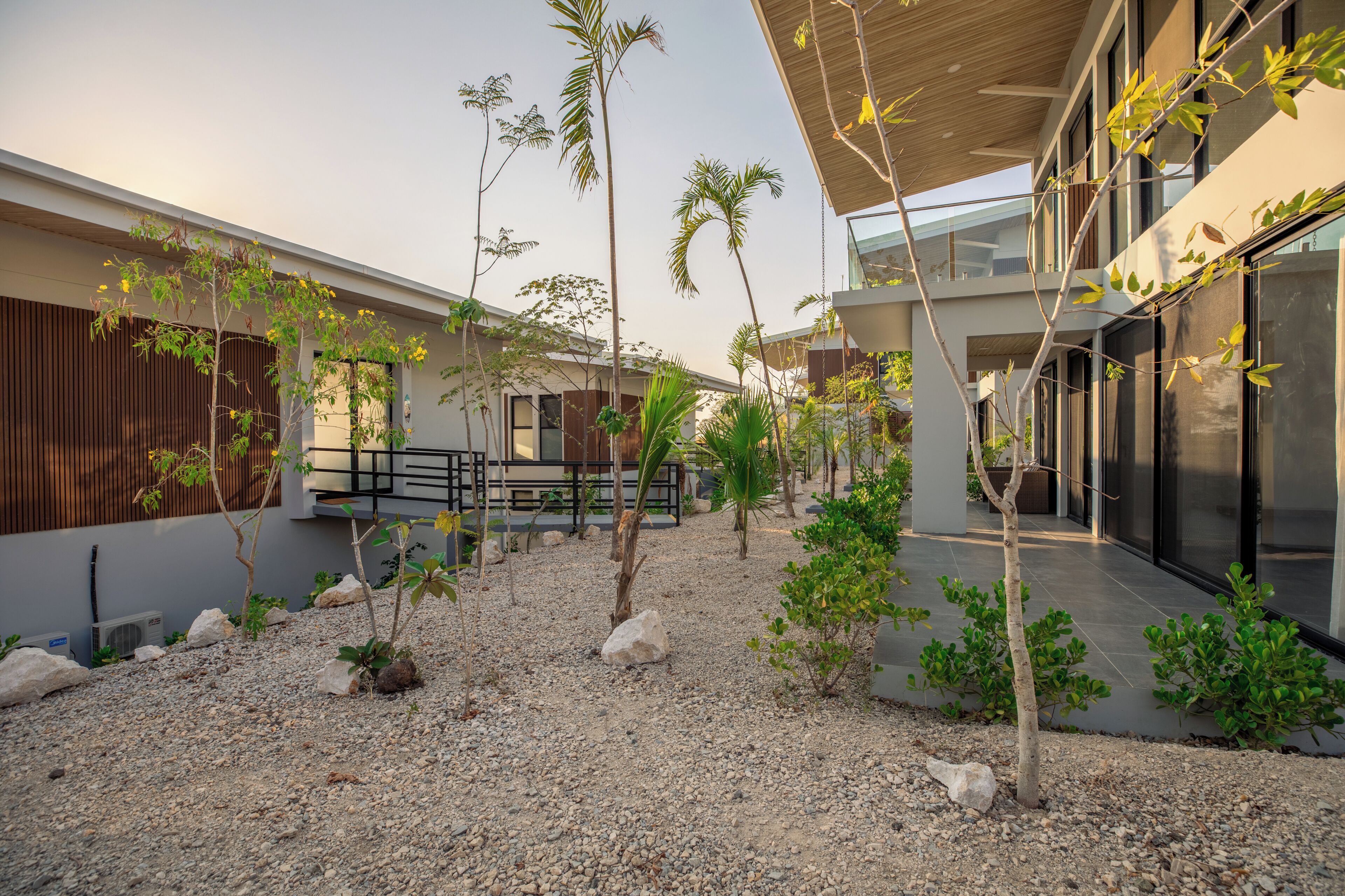 Un edificio moderno con un patio interior, que incluye una valla de madera, suelo de grava y diversas plantas.