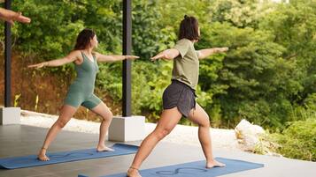 Deux personnes pratiquent le yoga sur des tapis à l’extérieur, avec une végétation luxuriante en arrière-plan.