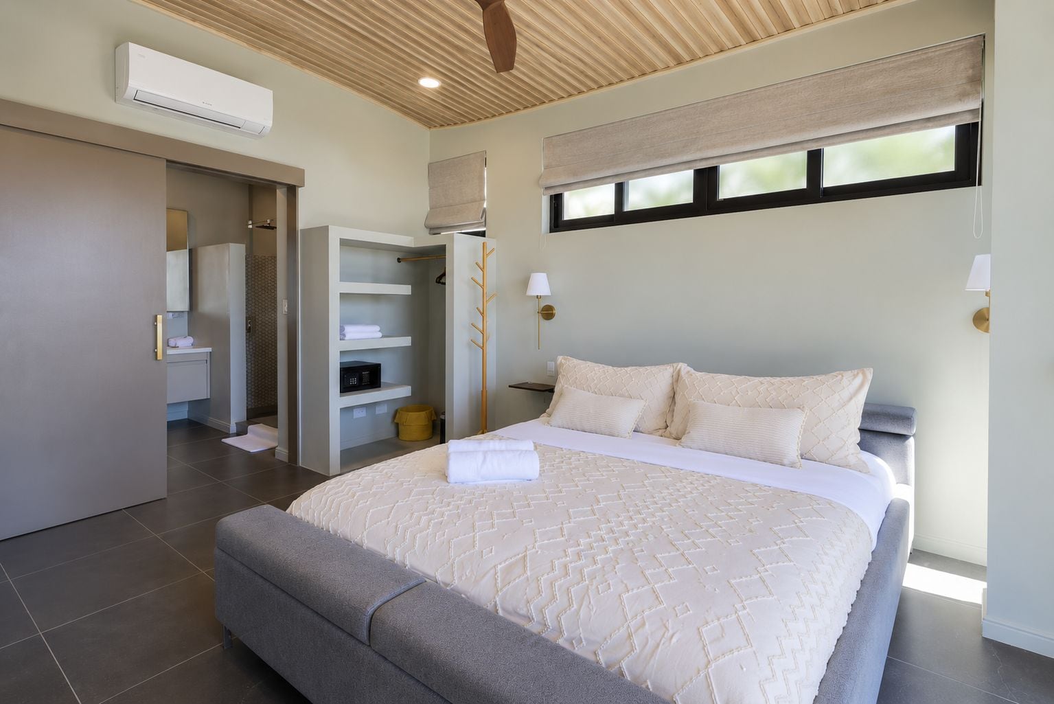 A bedroom with a large bed, a walk-in closet, a window with blinds, and a ceiling fan.