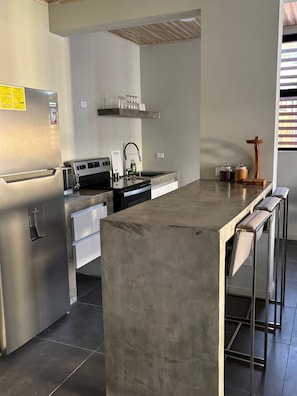 Ett modernt kök med ett kylskåp i rostfritt stål, en inbyggd ugn och en stor köksö med barstolar.