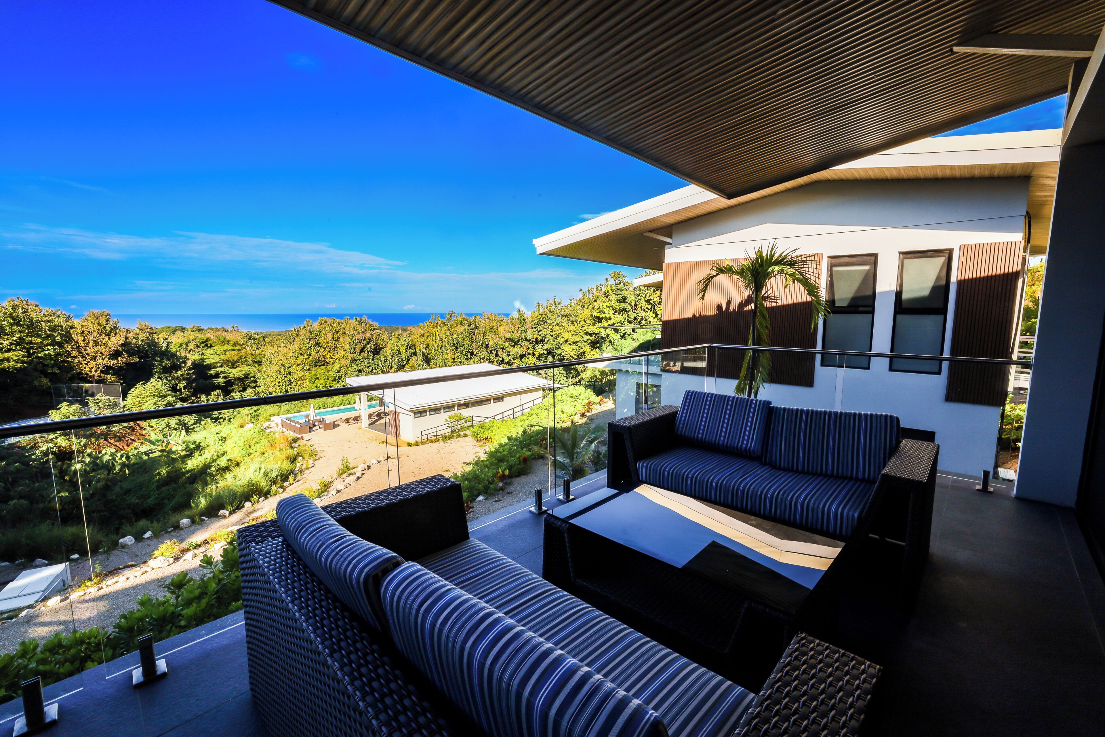A balcony with outdoor seating, a view of the ocean, and a modern building in the background.