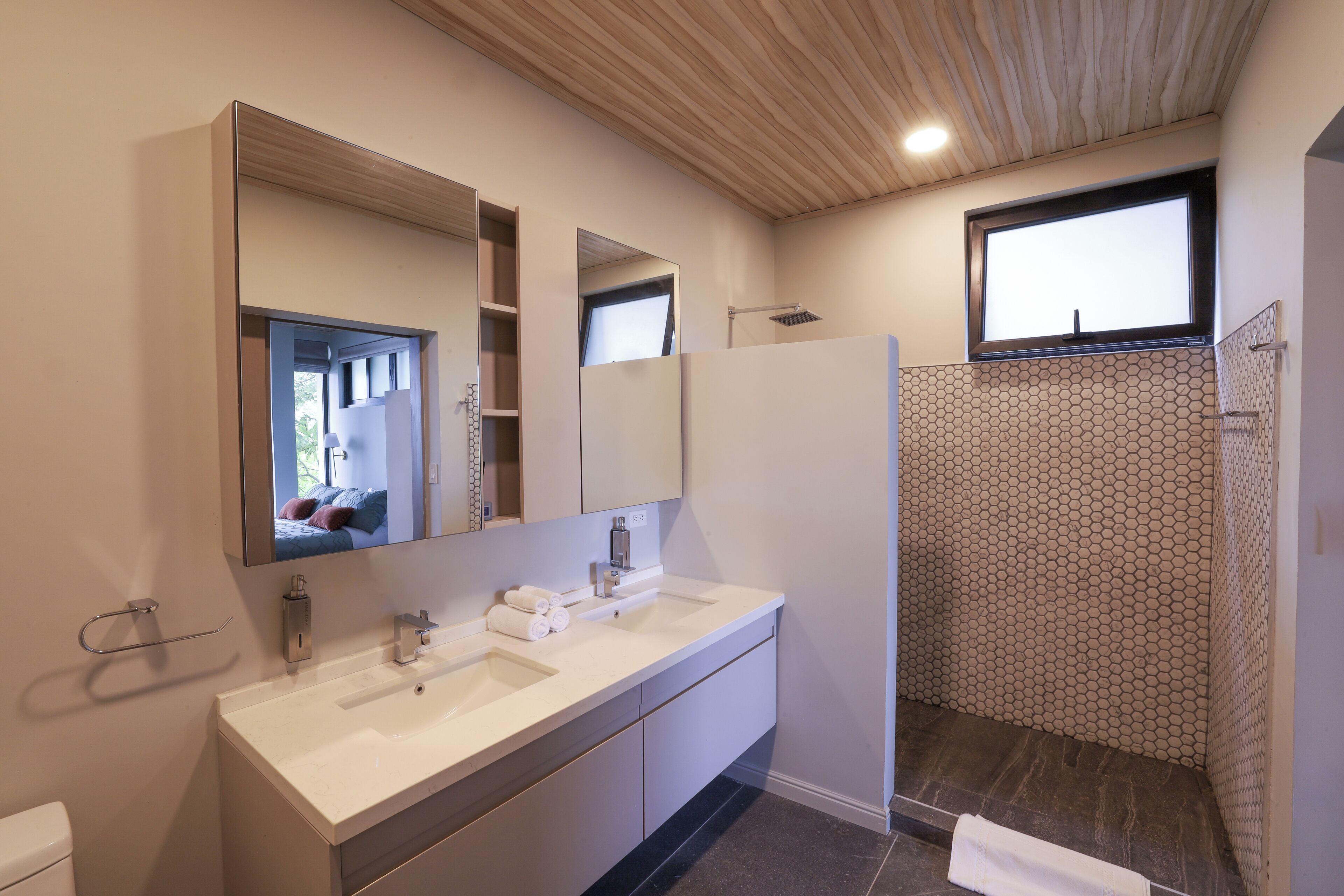 A modern bathroom with a large mirror, a shower, and a toilet.