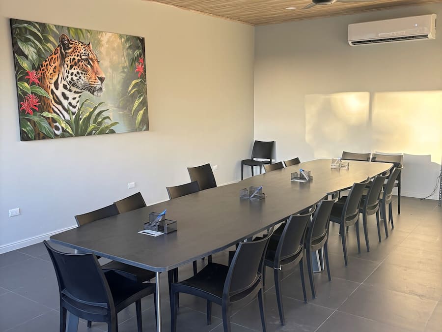 Un salón de conferencias con una larga mesa, sillas, ventiladores de techo y un equipo de aire acondicionado.