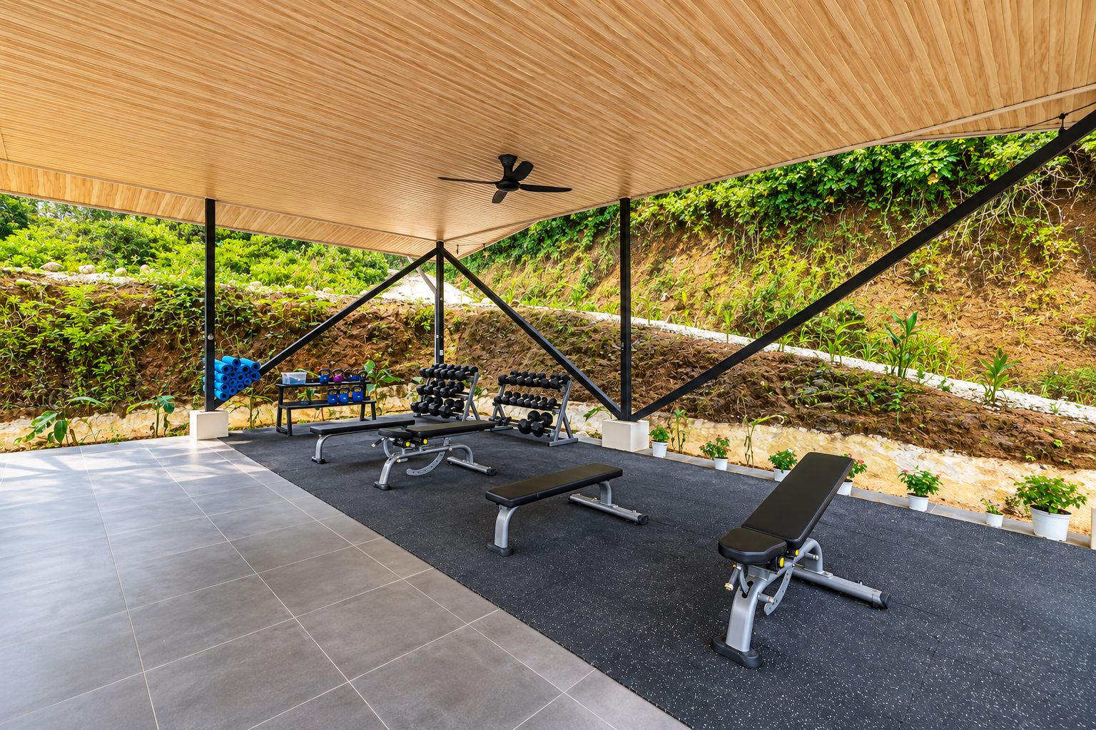 Un espace de remise en forme en plein air équipé d’appareils d’exercice, un espace de repos couvert et une vue sur un jardin aménagé.