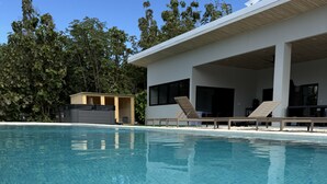 En klarblå pool med solstolar och en modern byggnad i bakgrunden.