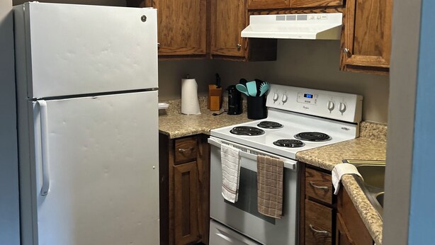 Una cocina con armarios de madera, un refrigerador blanco, una estufa y un microondas.